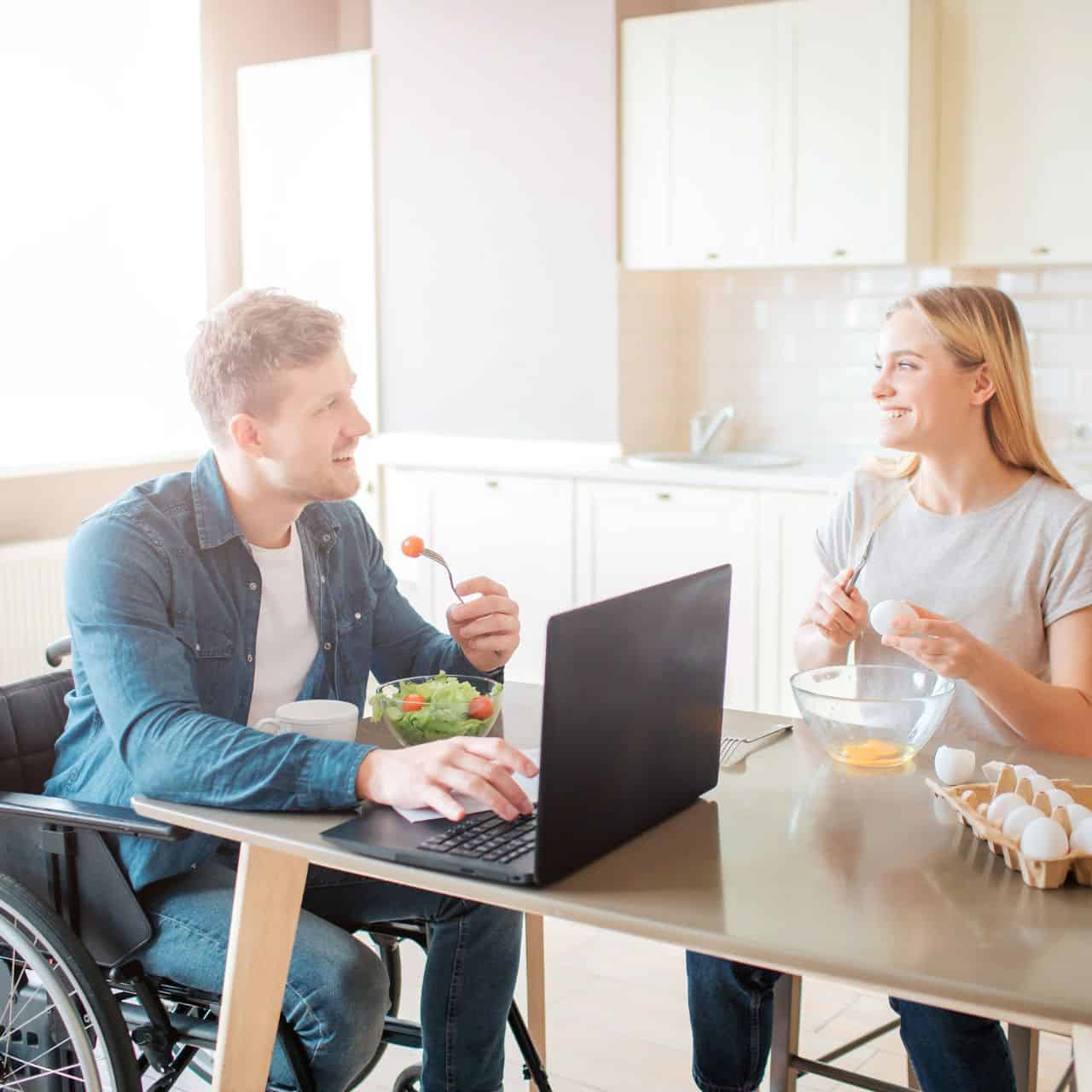 man in wheelchair eating with friend at table